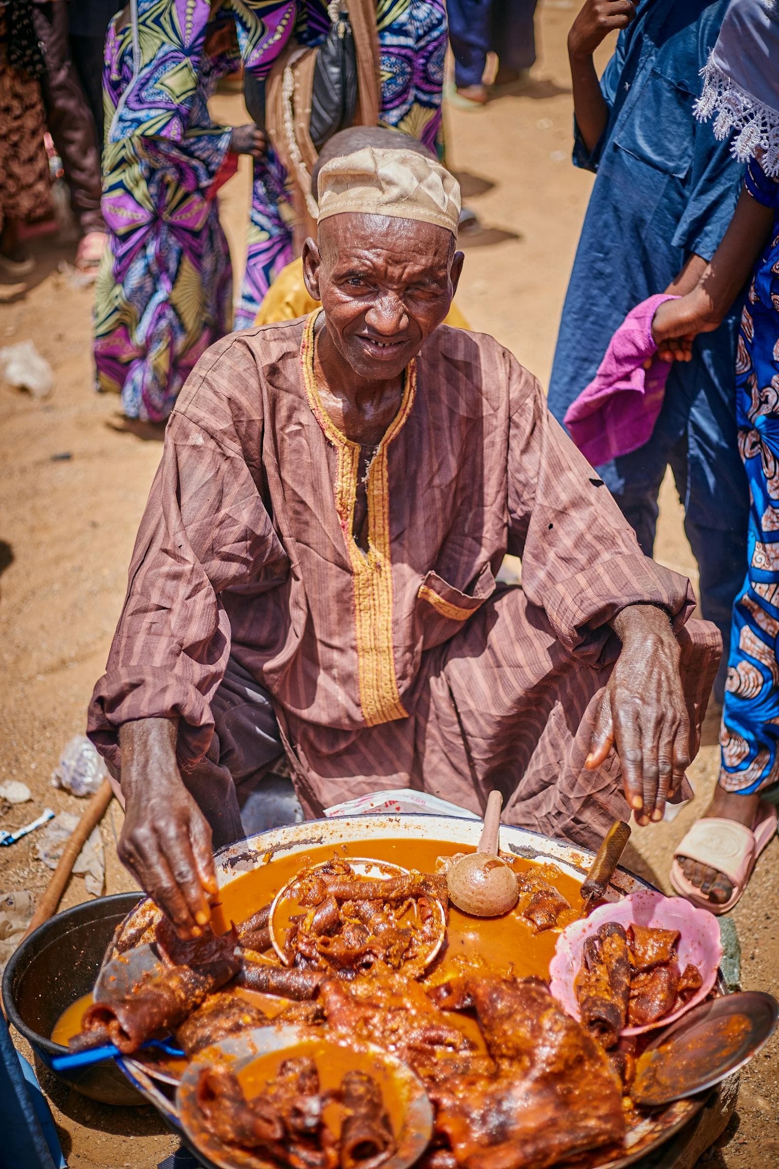 African food vendor serving customers at an outdoor market stall.